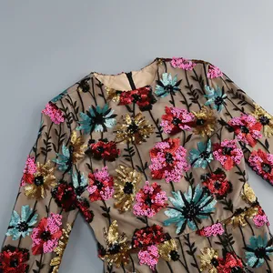 Close-up van een mesh-jurk met kleurrijke geborduurde bloemen van pailletten en een ronde hals.