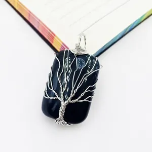 Vista detallada de un colgante de árbol de la vida hecho a mano con piedra negra y alambre envuelto.
