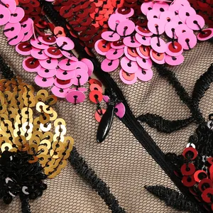 Gedetailleerde close-up van bloemen pailletten borduurwerk op zwarte mesh jurk met rits