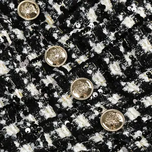 Primer plano de tela de tweed blanca y negra con lentejuelas y botones dorados grabados