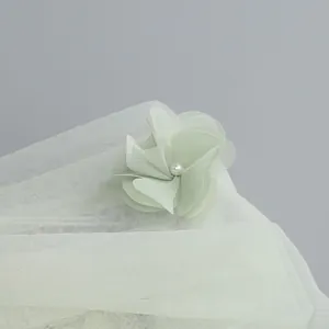 Detailed macro shot of a delicate 3D mesh flower with pearl on a sage green veil dress