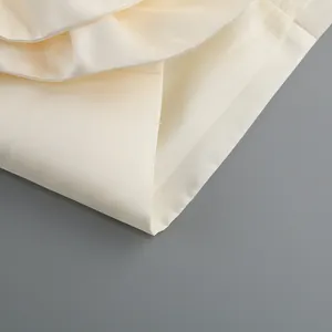Gros plan détaillé montrant la texture élégante du tissu crème et l'ourlet de la robe