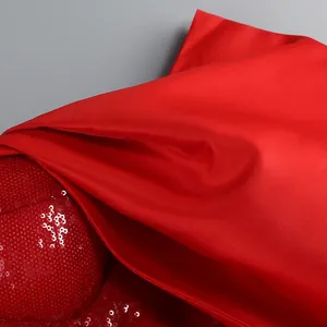 Dettaglio ravvicinato del tessuto di raso rosso e della trama di paillettes del vestito.