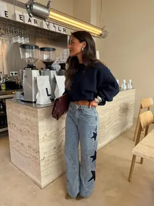 Woman in stylish light blue wide leg jeans with black star patchwork in a cafe setting.