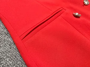 Gros plan d'une robe blazer rouge montrant le détail de la poche et des boutons argentés.