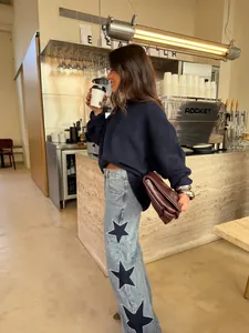 Women's loose straight denim jeans with large black star patches in coffee shop setting