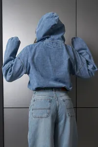 Vista posterior detallada de una chaqueta vaquera con capucha y corte holgado para mujer
