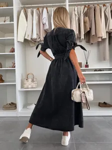 Back view of a long dark wash denim dress featuring tied sleeve details in a modern closet setting