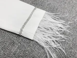 Gros plan d'une manche de blazer blanc avec strass et bordure en plumes d'autruche.
