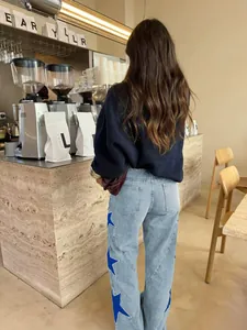 Womens light blue wide leg jeans with blue rhinestone star patches shown in a cafe setting
