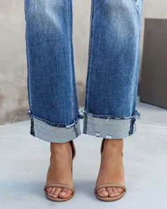 Detail of women's straight-leg washed jeans featuring cuffed frayed hems and tan sandals