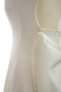 Close-up detail of white satin backless dress with elegant pearl trim and bow accent
