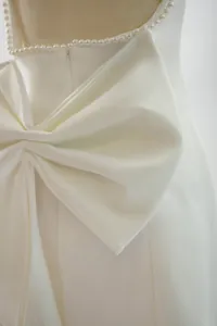 Detailed view of elegant white dress featuring large bow and pearl trim back detail.