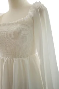 Detalle de vestido de hada blanco de manga larga con corpiño nido de abeja y volantes