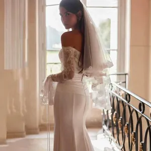Elegant off-shoulder fishtail wedding dress with delicate lace sleeves and a tiered veil.