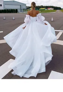 Close-up back view of a white gown with layered puff sleeves and flowing skirt train on runway.