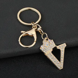 Macro detail view of a golden 'V' letter keychain charm with crown and sparkling rhinestones.