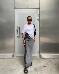 Vue complète d'un mannequin portant une jupe longue en satin gris devant un mur en métal