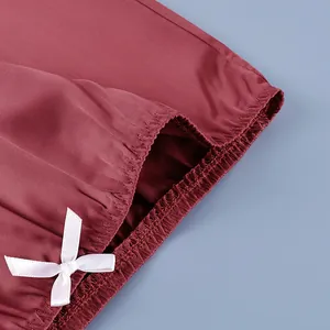 Close-up detail of a burgundy satin skirt featuring an elastic waistband and white bow accent