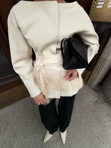 Detailansicht eines eleganten cremefarbenen Wickelrocks mit Fransen und weißem Blazer.