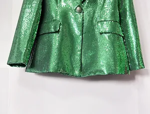 Detail shot of a green sequined blazer featuring a silver crest button and flap pockets.
