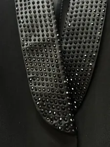 Dettaglio ravvicinato di un bavero a scialle di un blazer nero con strass neri luccicanti.