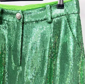 Detail of emerald green sequined trousers showing high-waist and crest-embossed button.