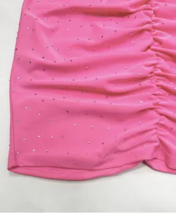 Detailed close-up showing hot-fix rhinestones on pink ruched elastic knit fabric