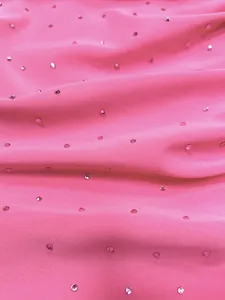 Close-up detail of pink stretch knit fabric with scattered hot-fix rhinestones.