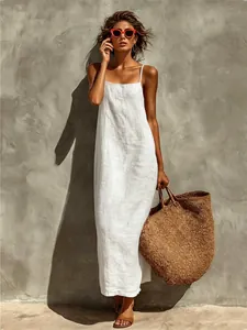 Modèle portant une robe longue en lin blanc avec un sac tissé dans un décor d'été