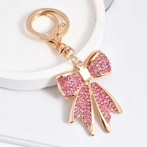Close-up detail of an elegant gold-tone metal keychain featuring a sparkling pink rhinestone bow charm.