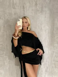 Vista completa del crop top nero con spalle scoperte e del set minigonna coordinato.