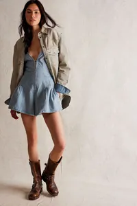 Full body shot of light blue denim romper styled with beige jacket and brown vintage boots