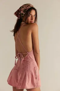Back view detail of a pink denim romper with crisscross straps and open back.