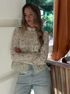 Close-up of elegant white lace high-neck blouse with floral embroidery and button details.