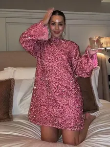 Model wearing a pink sequined long-sleeved mini dress in a cozy bedroom lifestyle scene