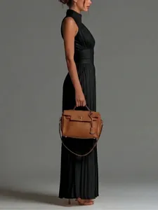 Side profile of a woman wearing a black pleated halter jumpsuit and holding a tan handbag