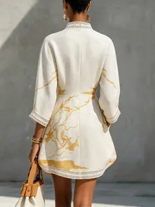 Close-up back view of a white linen mini dress with gold abstract print and lace trim