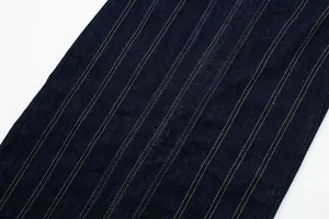 Close-up detail of dark blue denim fabric texture with elegant gold contrast stitching