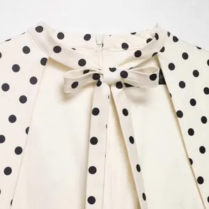 Detailed view of elegant white sleeveless dress featuring black polka dots and a bow collar