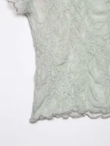 Close-up detail of vintage sage green flocked lace fabric with ruffled scalloped edges