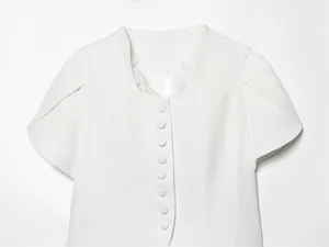 Detail view of a white short-sleeved blazer featuring lace trim and elegant fabric