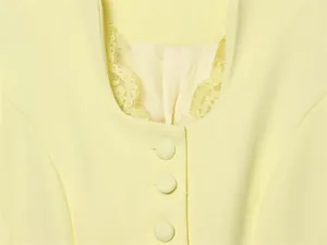 Detailed view showing the elegant lace-trimmed neckline and covered buttons on a yellow blazer