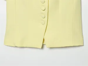 Close-up detail of a pale yellow suit jacket featuring fabric-covered buttons and hem slit.