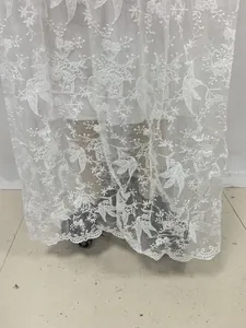 Vue détaillée d'une broderie de dentelle florale blanche complexe sur l'ourlet d'une robe de mariée.