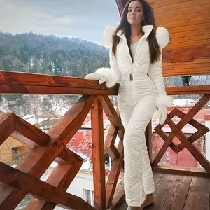 Full body shot of a stylish white one-piece ski suit with fur trim on a wooden balcony.