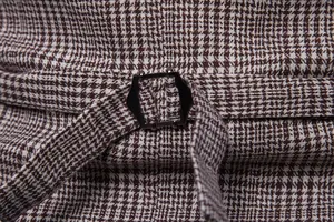 Macro view of adjustable dark metal cinch buckle on brown houndstooth men's suit vest