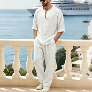 Dettaglio di un set in lino bianco con top a V indossato da un modello su un balcone sul mare.