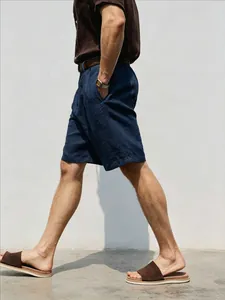 Side profile of a man walking wearing loose navy blue linen shorts with casual sandals