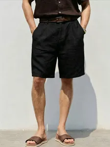 A detailed view of men's loose black linen shorts styled with a casual woven belt